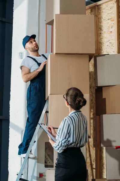 Empresária enchendo checklist enquanto carregador homem de pé em uma escada — Fotografia de Stock