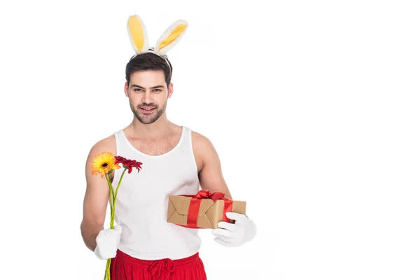 Mann mit Hasenohren hält Blumen und Geschenkbox isoliert auf weißem, Osterkonzept — Stockfoto