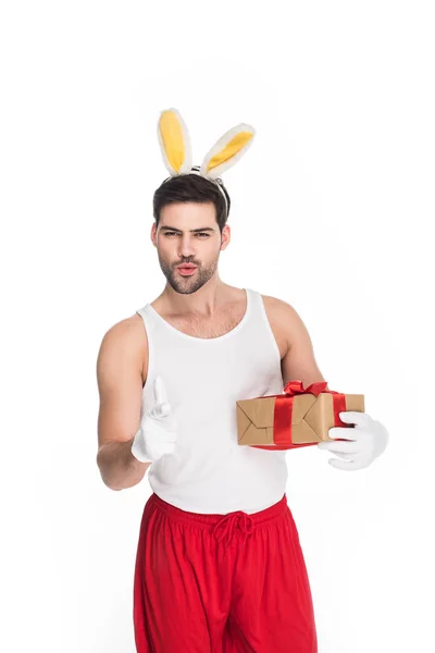 Sonriente hombre señalando con el dedo y sosteniendo caja de regalo aislado en blanco, concepto de Pascua - foto de stock