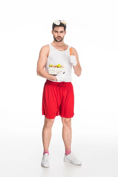 Hombre con orejas de conejo sosteniendo canasta de frutas y zanahoria aislado en blanco, concepto de Pascua - foto de stock