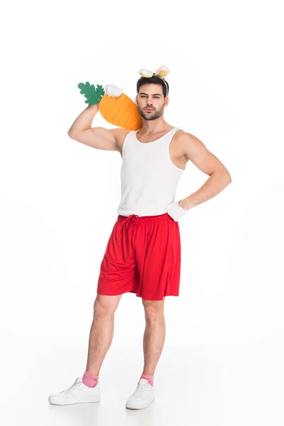 View of man with bunny ears holding big carrot on shoulder isolated on white, easter concept — Stock Photo