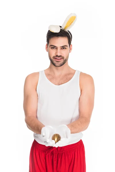 Homme souriant avec des oreilles de lapin tenant oeuf d'or isolé sur blanc, concept de Pâques — Stock Photo