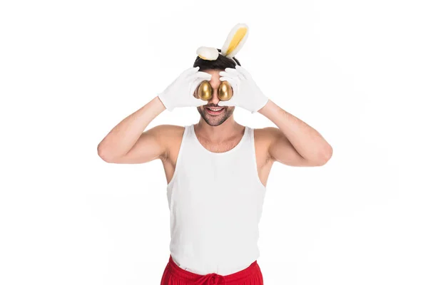 Young man with bunny ears closing eyes by golden eggs isolated on white, easter concept — Stock Photo