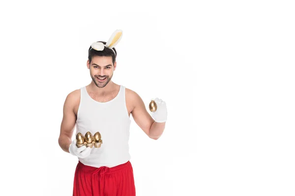 Lächelnder Mann mit Hasenohren mit goldenen Eiern auf weißem Osterkonzept — Stockfoto