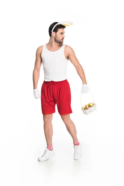 Hombre con orejas de conejito llevando cesta de frutas aisladas en el concepto blanco, pascua - foto de stock