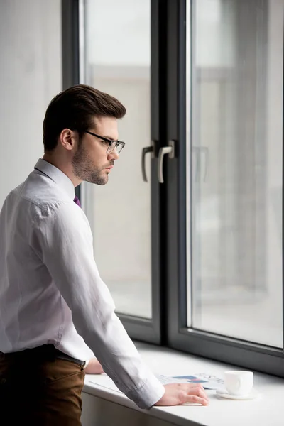 Profile of businessman in glasses with coffee cup and newspaper on window sill — Stock Photo