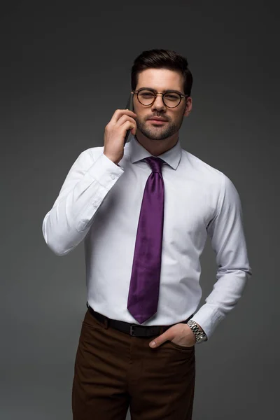 Lächelnder Geschäftsmann mit Brille im Gespräch auf Smartphone isoliert auf grau — Stockfoto