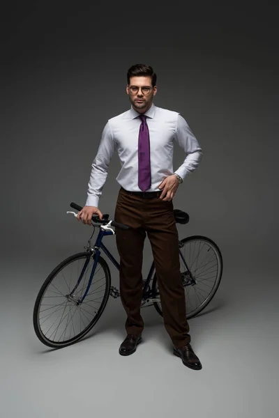 Vista frontal del hombre de negocios de pie con bicicleta en gris - foto de stock