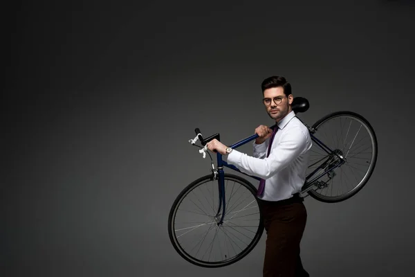 Jeune homme d'affaires en lunettes tenant le vélo dans les mains isolées sur gris — Stock Photo
