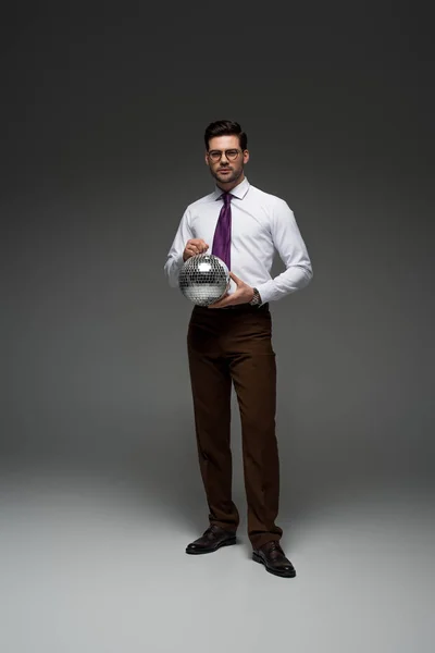 Young businessman in glasses holding glass disco ball on grey — Stock Photo