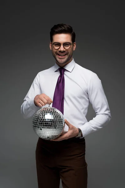 Sonriente hombre de negocios sosteniendo bola disco de vidrio aislado en gris - foto de stock