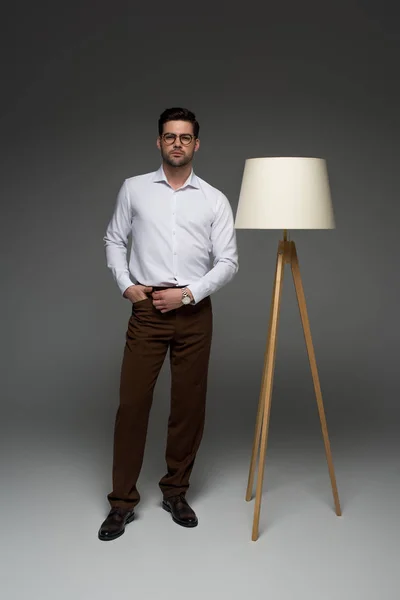 Vista frontal del hombre de negocios de pie con lámpara de pie al lado en gris - foto de stock