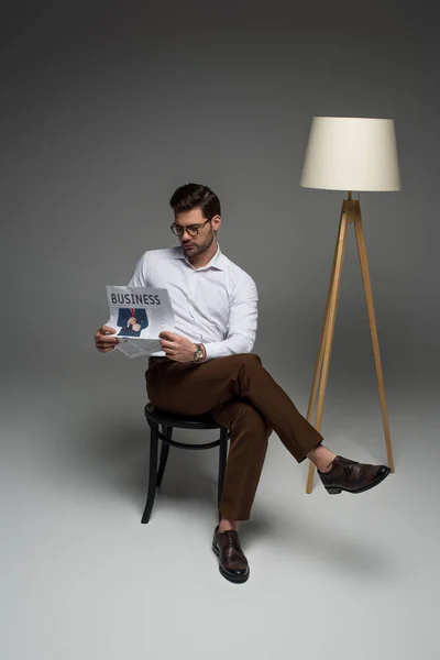 Jeune homme d'affaires assis sur une chaise et lisant un journal sur gris — Photo de stock