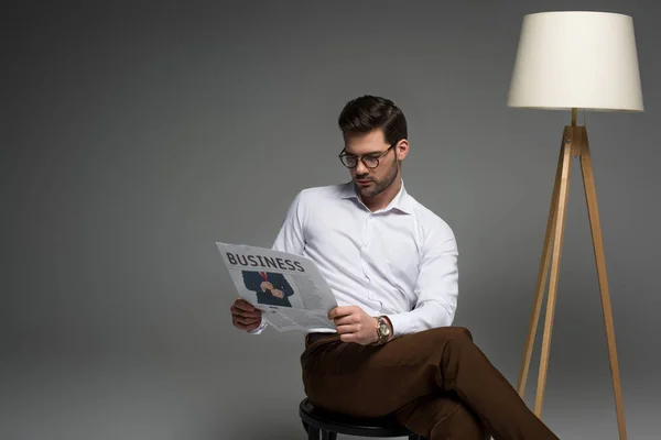 Stilvoller Geschäftsmann liest Zeitung in der Nähe von Stehlampe isoliert auf grau — Stockfoto