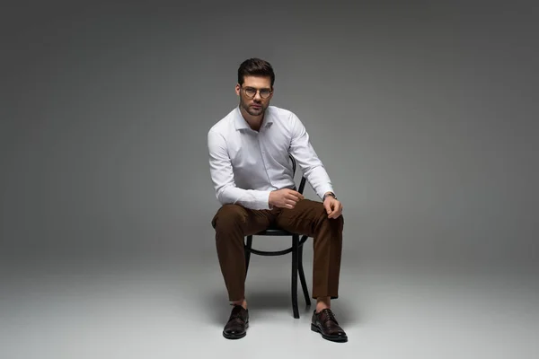 Stylish businessman in glasses sitting on grey — Stock Photo
