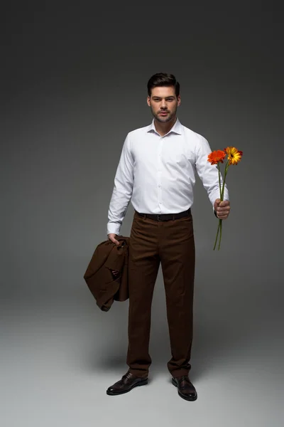 View of  stylish businessman holding bouquet of flowers on grey — Stock Photo