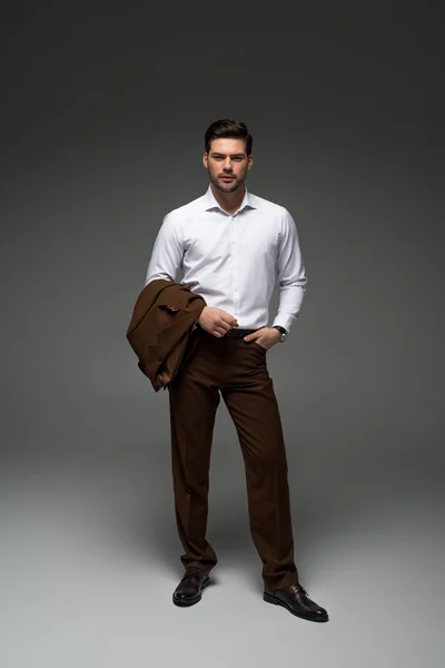 Elegante uomo d'affari in piedi con giacca su una mano su grigio — Foto stock