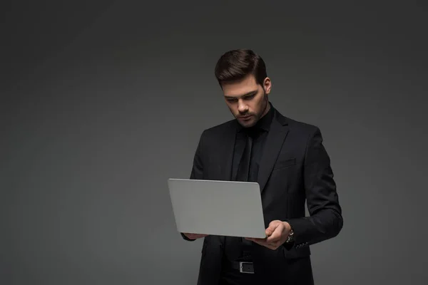 Elegante hombre de negocios sosteniendo portátil aislado en gris - foto de stock