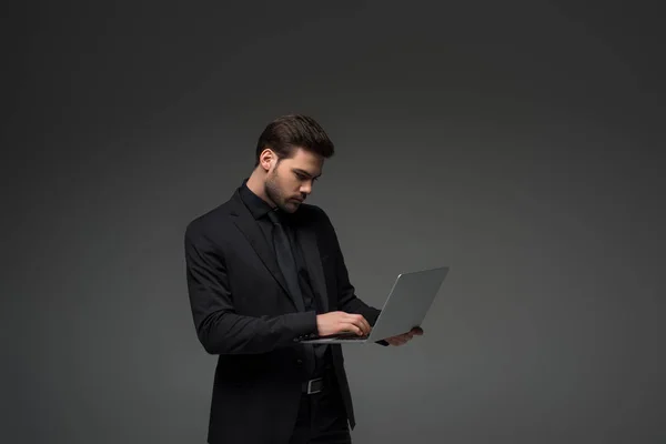 Vue latérale de l'homme d'affaires tapant sur ordinateur portable isolé sur gris — Photo de stock