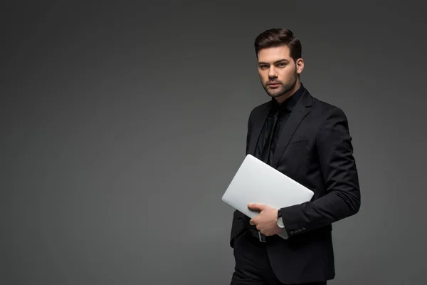 Retrato de joven empresario con portátil en manos aisladas en gris - foto de stock