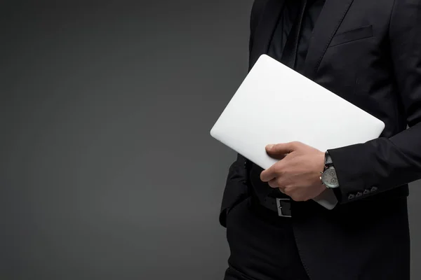 Частичный взгляд бизнесмена, держащего ноутбук в руке изолирован на сером — стоковое фото