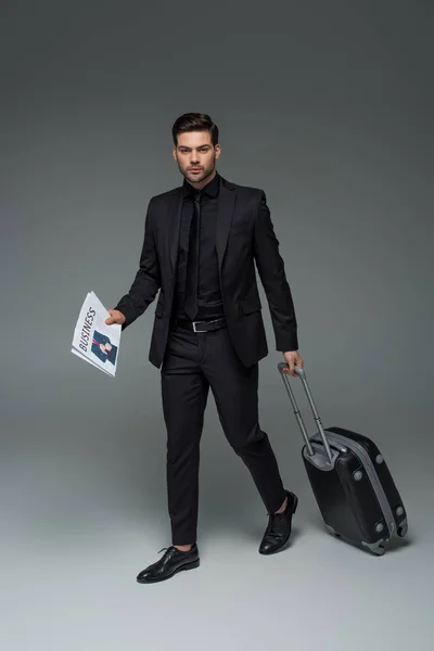 Business tourist with newspaper carrying suitcase on grey — Stock Photo