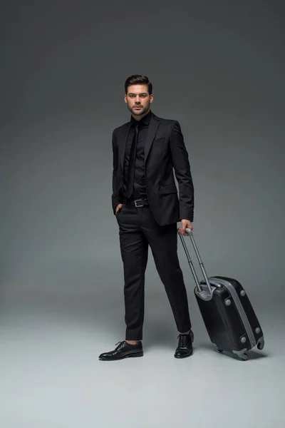 Joven turista elegante que lleva la maleta en gris - foto de stock