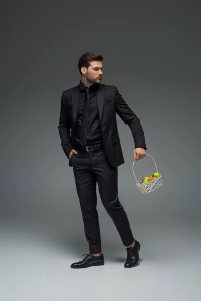 Молодий бізнесмен, що носить кошик фруктів на сірому — стокове фото