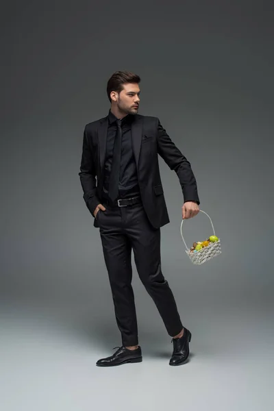 Joven empresario llevando canasta de frutas en gris - foto de stock