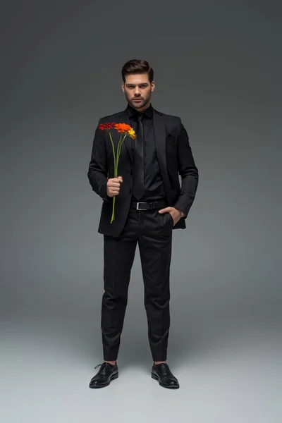 Joven macho sosteniendo ramo de flores en gris, concepto de día internacional de la mujer - foto de stock