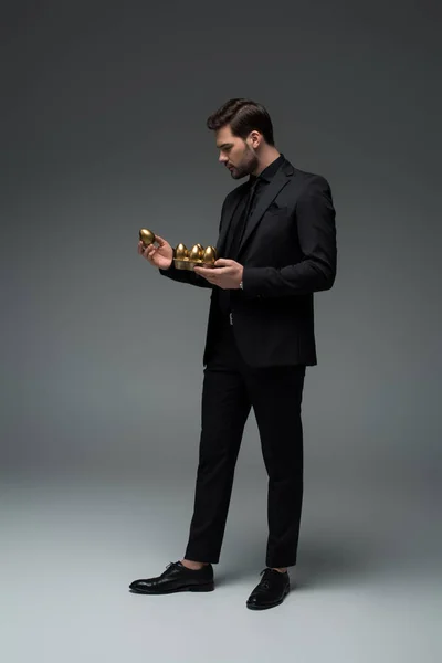 Side view of stylish male holding golden eggs on grey, easter concept — Stock Photo