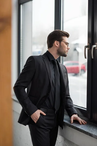 Vista lateral de un joven hombre de negocios mirando por la ventana - foto de stock