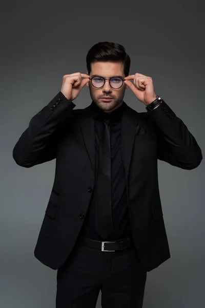 Hombre de elegante traje negro quitándose las gafas aisladas en gris - foto de stock