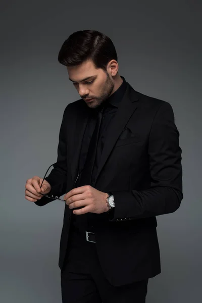 Stylish man in black suit holding glasses isolated on grey — Stock Photo