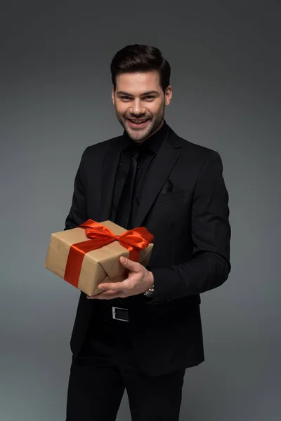 Jovem sorrindo macho em terno formal segurando caixa de presente isolado em cinza, conceito de dia internacional das mulheres — Fotografia de Stock