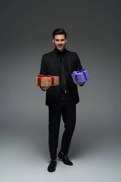 Smiling young man in suit holding two gift boxes on grey, international womens day concept — Stock Photo