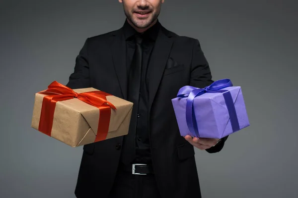 Vista recortada del macho en traje negro sosteniendo dos cajas de regalo aisladas en gris, concepto de día de la mujer internacional - foto de stock