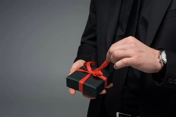 Vista parcial de la mano masculina desatando la cinta en la caja de regalo aislado en gris, concepto de día internacional de la mujer - foto de stock