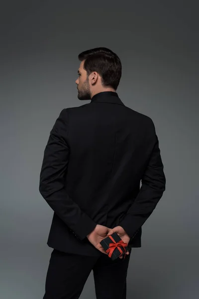 Вид ззаду стильний чоловік тримає подарункову коробку ізольовано на сірому, міжнародному жіночому концепті дня — стокове фото