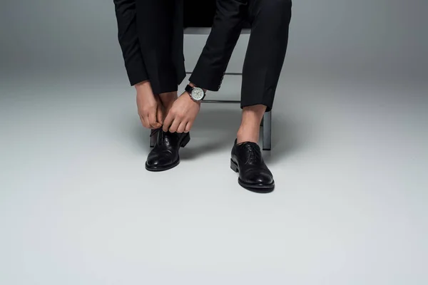 Partial view of stylish man tying shoelaces on grey — Stock Photo