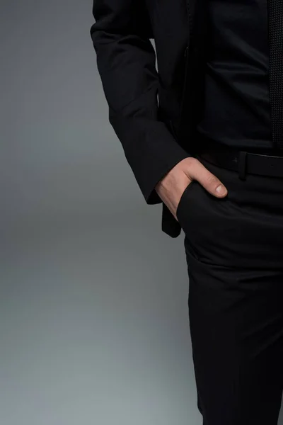Vista parcial de mano masculina en bolsillo de traje negro aislado en gris - foto de stock