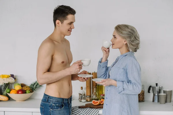 Shirtless boyfriend and girlfriend in unbuttoned shirt drinking coffee in morning — Stock Photo