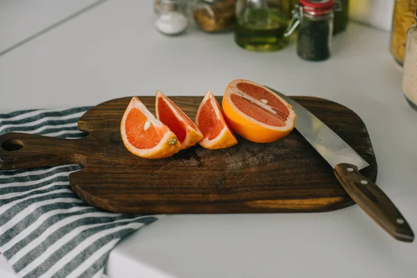 Cut grapefruit with knife on wooden board in kitchen — Stock Photo