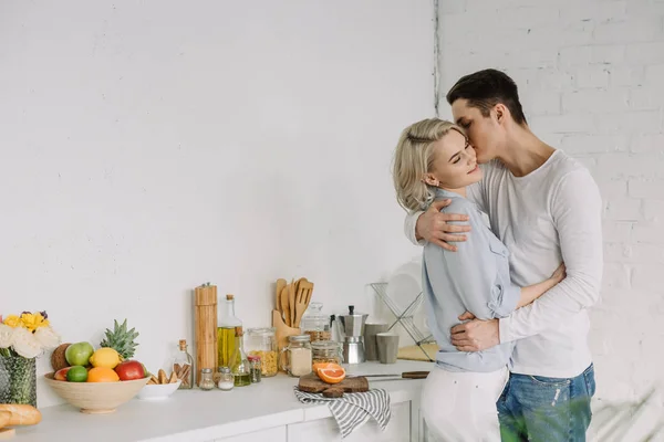 Парень обнимает и целует девушку на кухне — стоковое фото