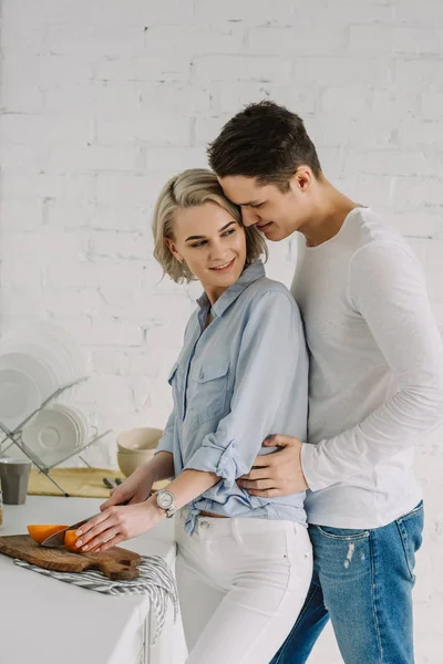 Novio abrazando novia corte pomelo en la cocina - foto de stock