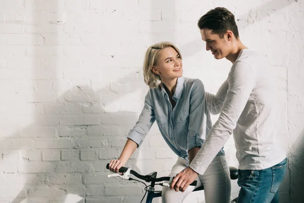 Novio abrazando novia sentado en bicicleta en casa - foto de stock