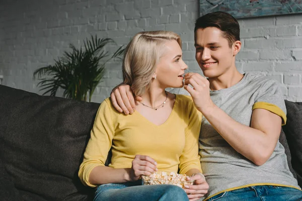 Fidanzato felice alimentazione fidanzata con popcorn sul divano — Foto stock