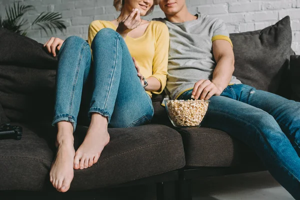 Imagen recortada de pareja sentada en un sofá con palomitas de maíz - foto de stock