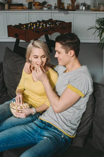 Boyfriend feeding girlfriend with popcorn at home — Stock Photo