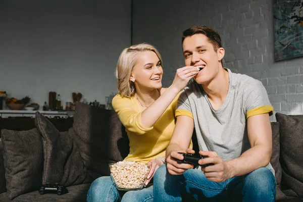 Sorrindo namorada alimentando namorado com pipocas em casa — Fotografia de Stock
